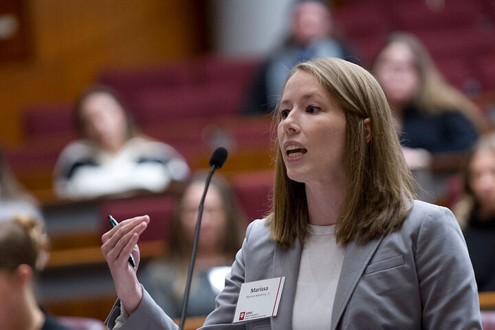 A female law student stands at a podium in a moot court setting.